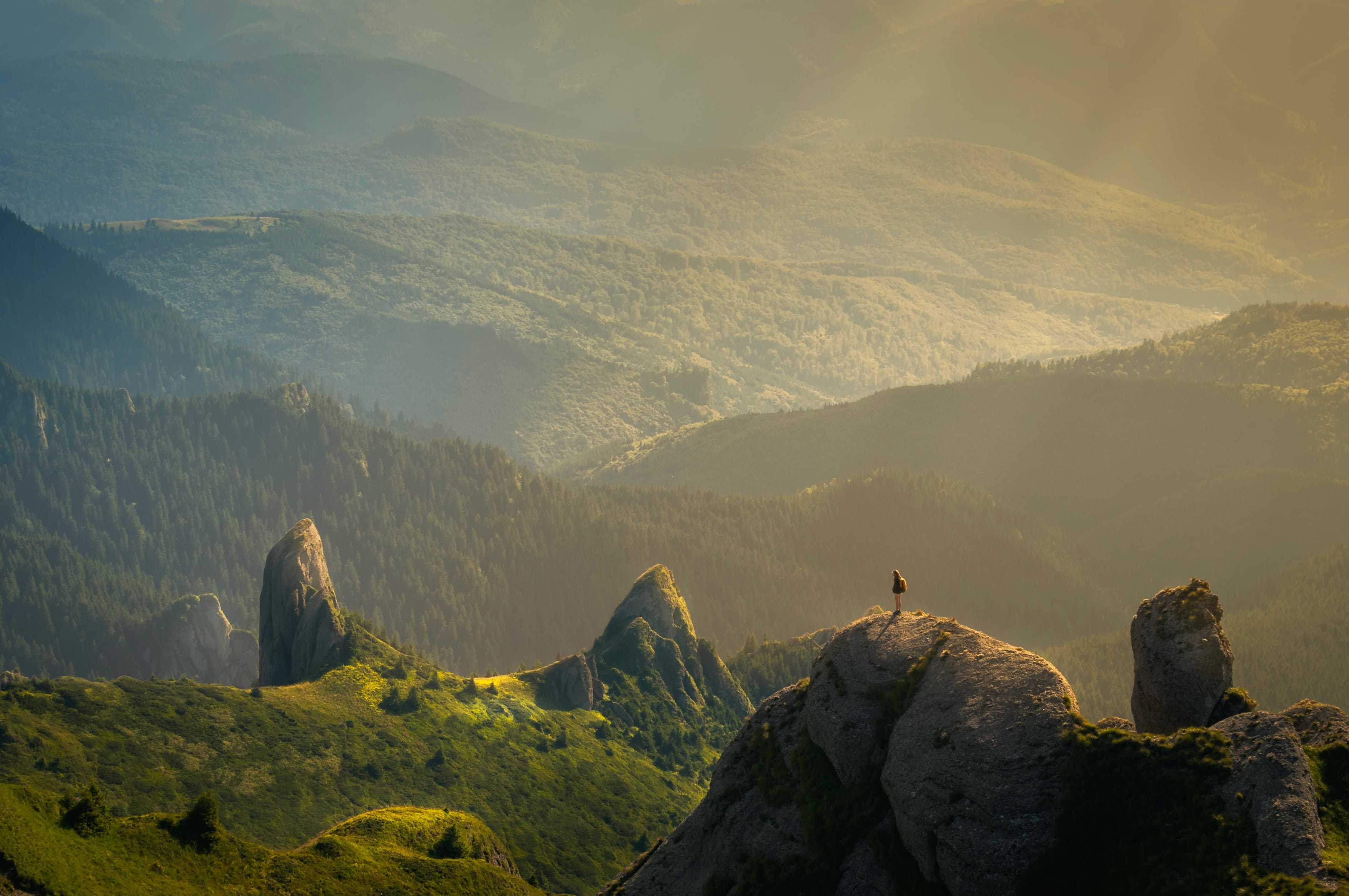 Sunny, green hills and a person with a backpack standing on a cliff, perhaps envisioning a sustainble future?